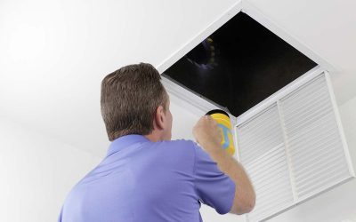 Older male with a yellow flashlight examining HVAC ducts in a large square vent. Male technician looking over the air ducts inside a home air intake vent.